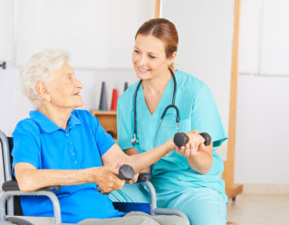 caregiver assisting elderly woman in using dumbbell