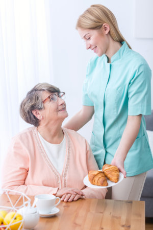 caregiver preparing bread for elderly woman